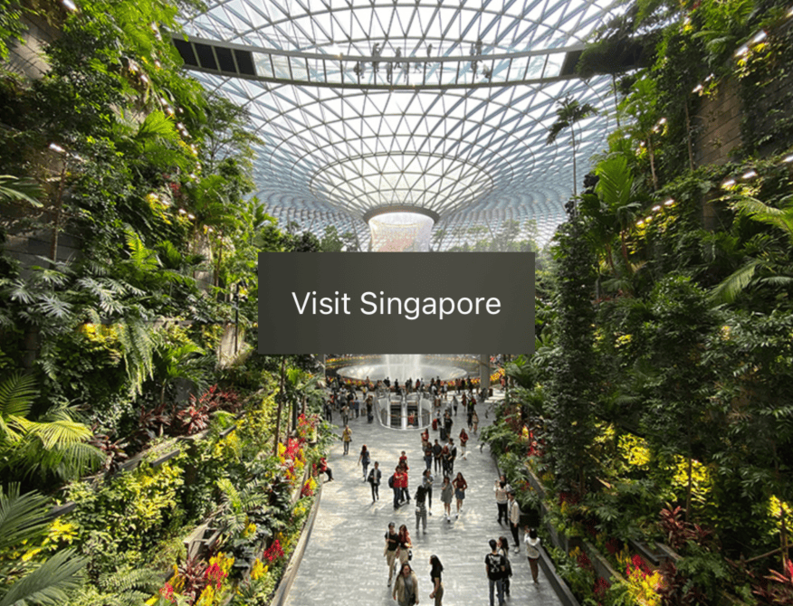 The words “Visit Singapore” on a grey rectangle over an image of Singapore's Jewel indoor waterfall. The rectangle has a slightly translucent frosted glass effect.
