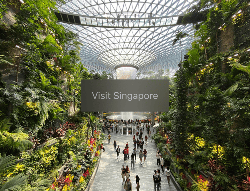 The words “Visit Singapore” in grey on a rectangle over an image of Singapore's Jewel indoor waterfall. The rectangle has a translucent frosted glass effect.